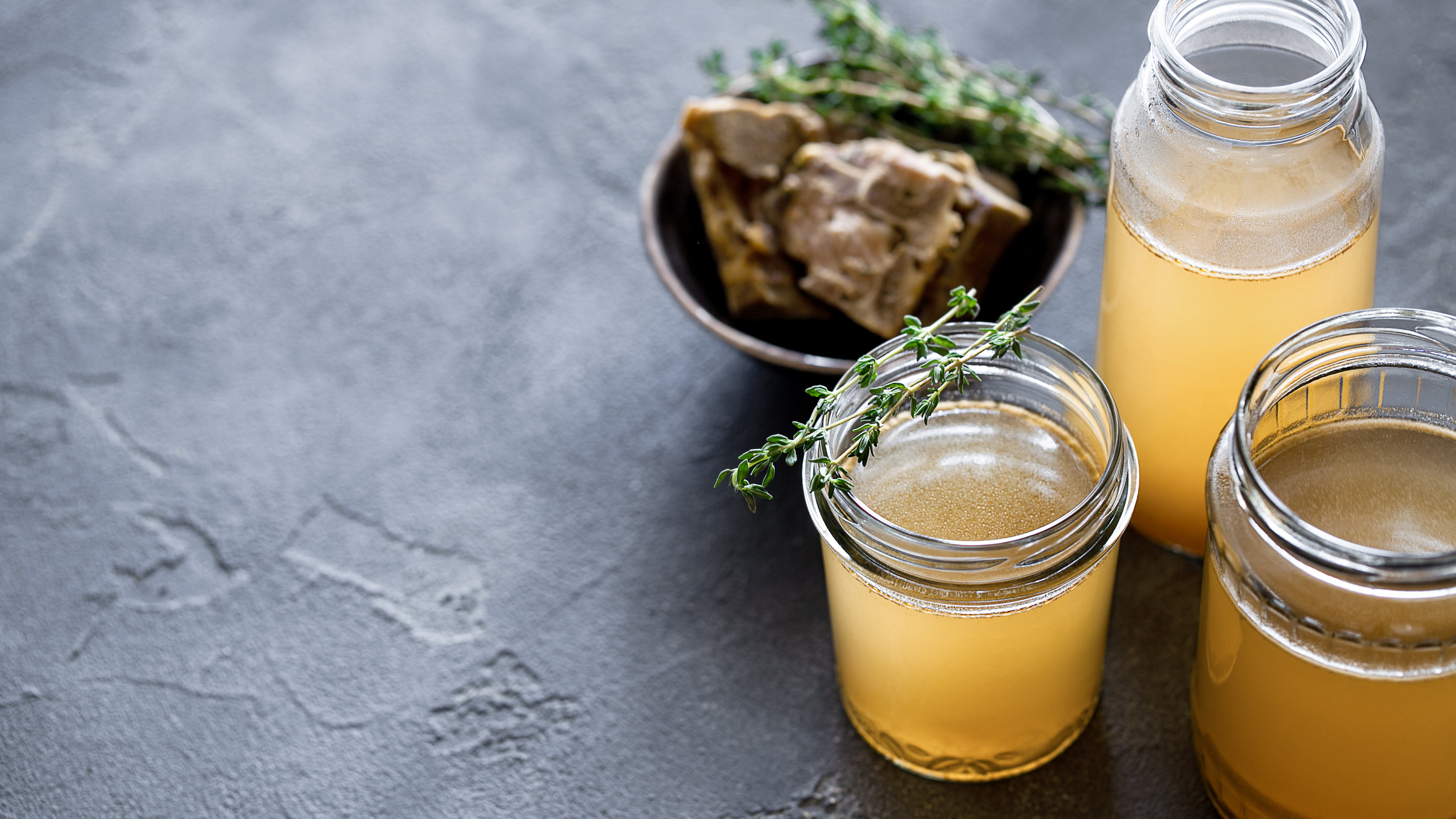 Glass jar with yellow fresh bone broth on dark gray background